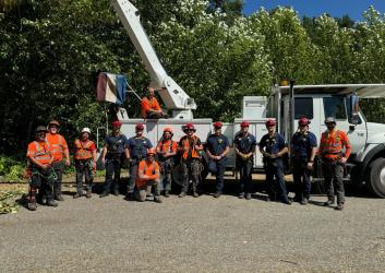 A group of men, some in orange vests, stand in front of a bucket truck.
